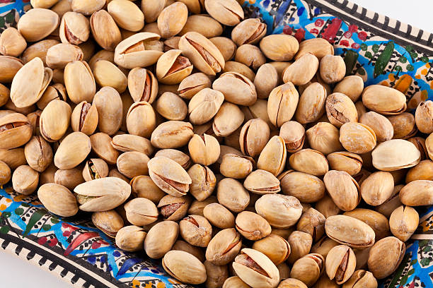A bunch of pistachios in a colorful, African, ceramic dish.